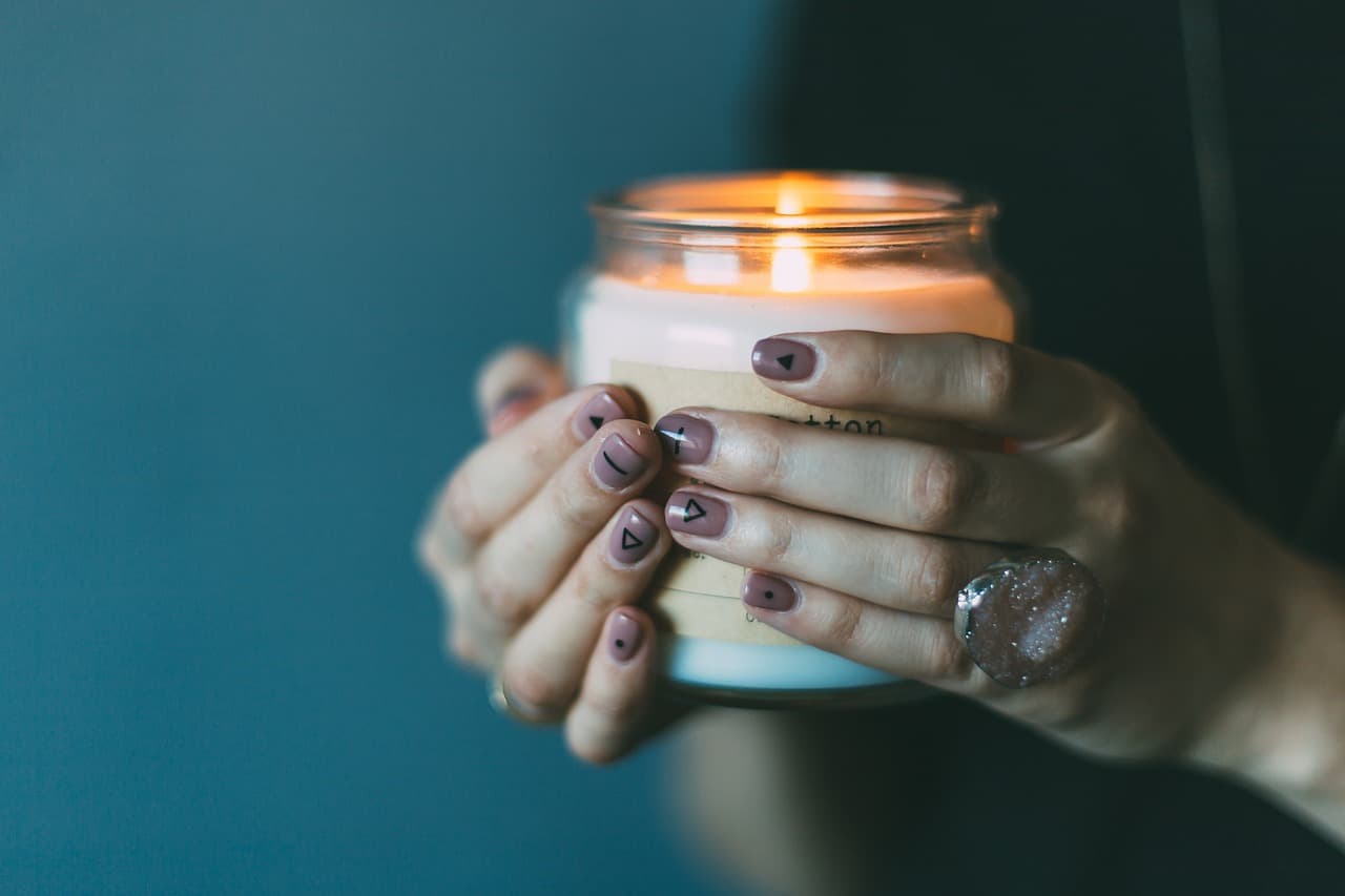 Hands with a mauve manicure holding a lit candle