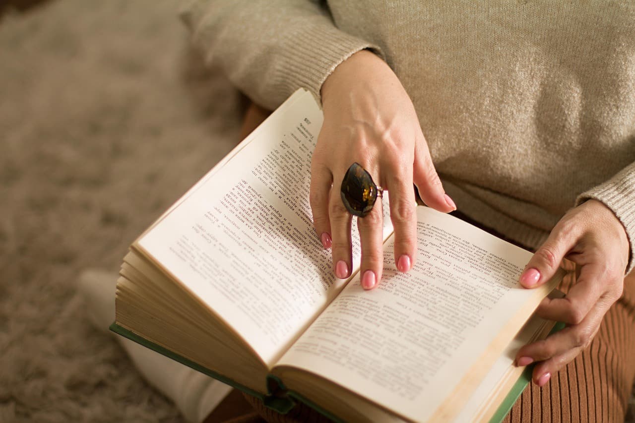 Natural pink nails on hands holding an open book